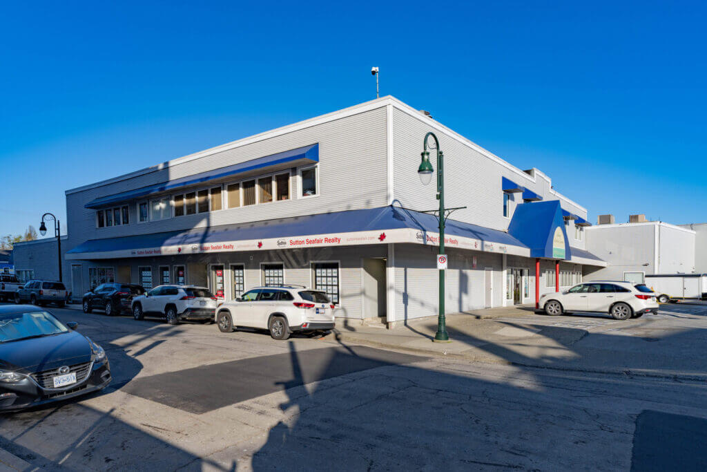 Street-level exterior of Ladner Harbour Centre showing retail storefronts and blue canopy